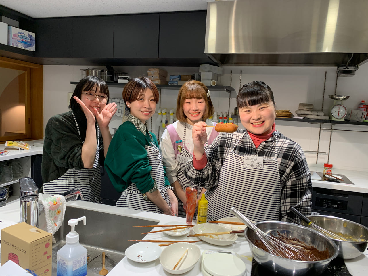 ▲みんなも食べます。左から２番目がみのもまりかさん、アメリカンドッグを持っているのがはっとりかんなさん。