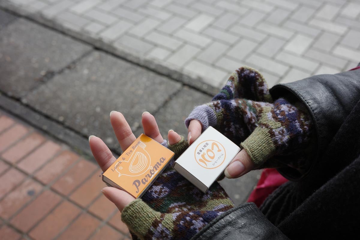 鳥の看板がモチーフのマッチを手に持っています。