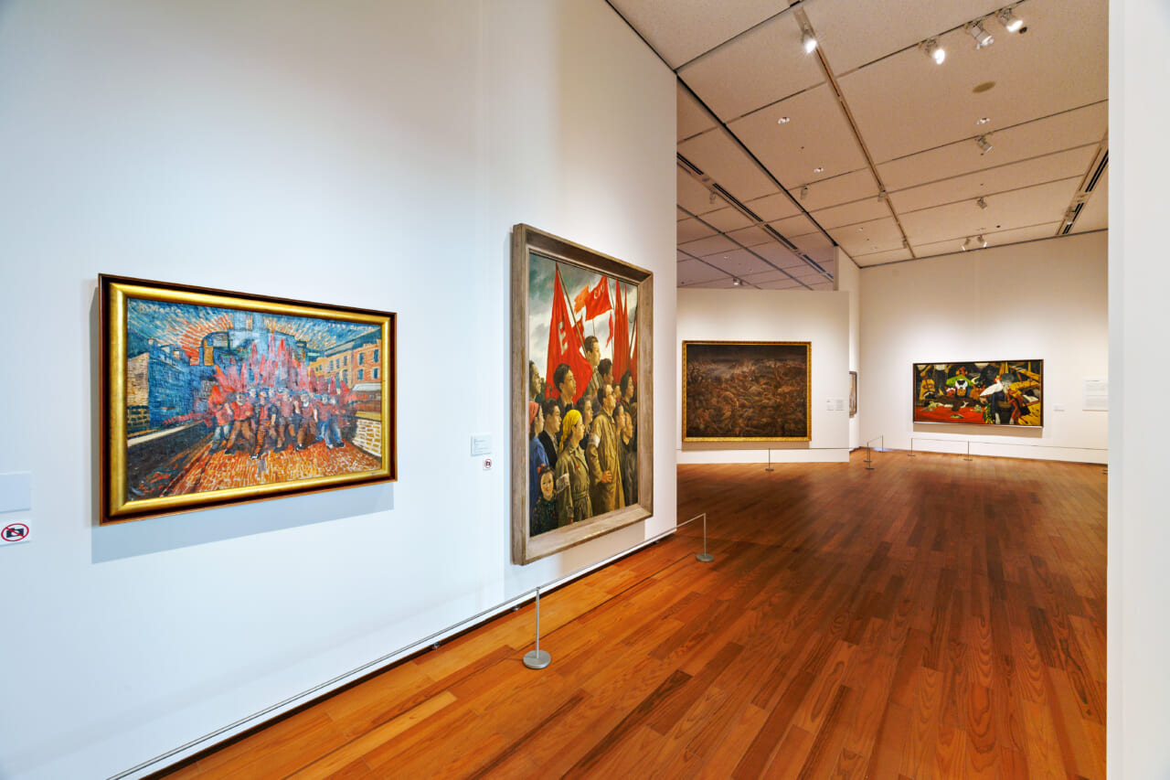 左手の壁・右側：内田巌《歌声よ起これ（文化を守る人々）》　その奥に藤田嗣治《アッツ島玉砕》が見える。開館記念展 アート・オブ・ザ・リアル  第５章 会場風景