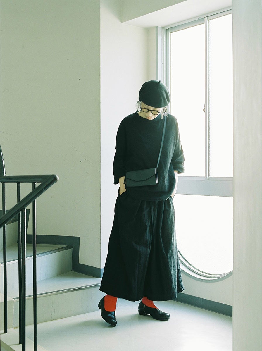 黒いベレー帽に黒い服を纏った女性が、おさいふショルダーを身につけている。差し色に赤い靴下。