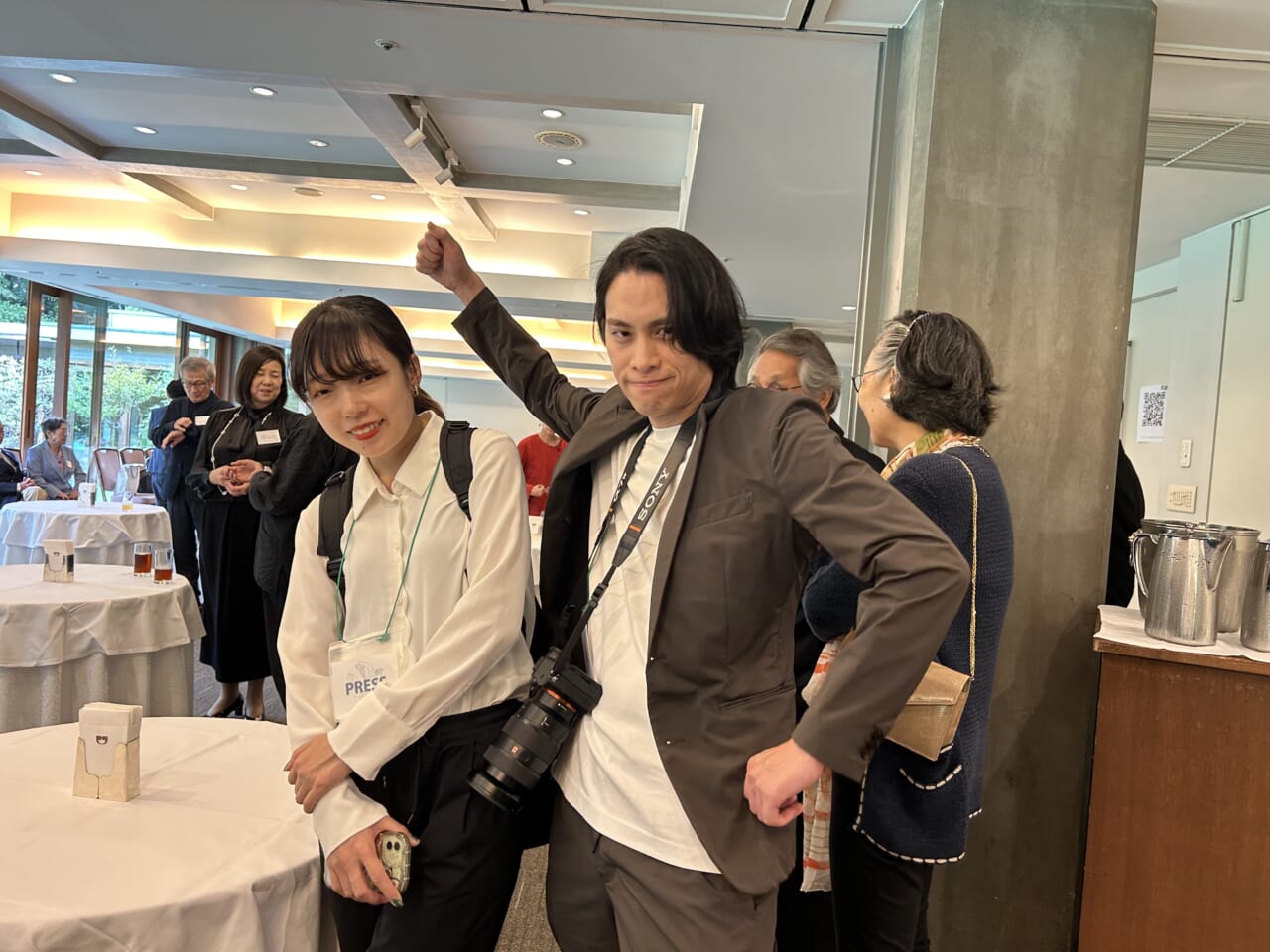 伊丹十三賞贈呈式の会場で、カメラをさげてガッツポーズをするサノさんと、へなへな立っている松本。