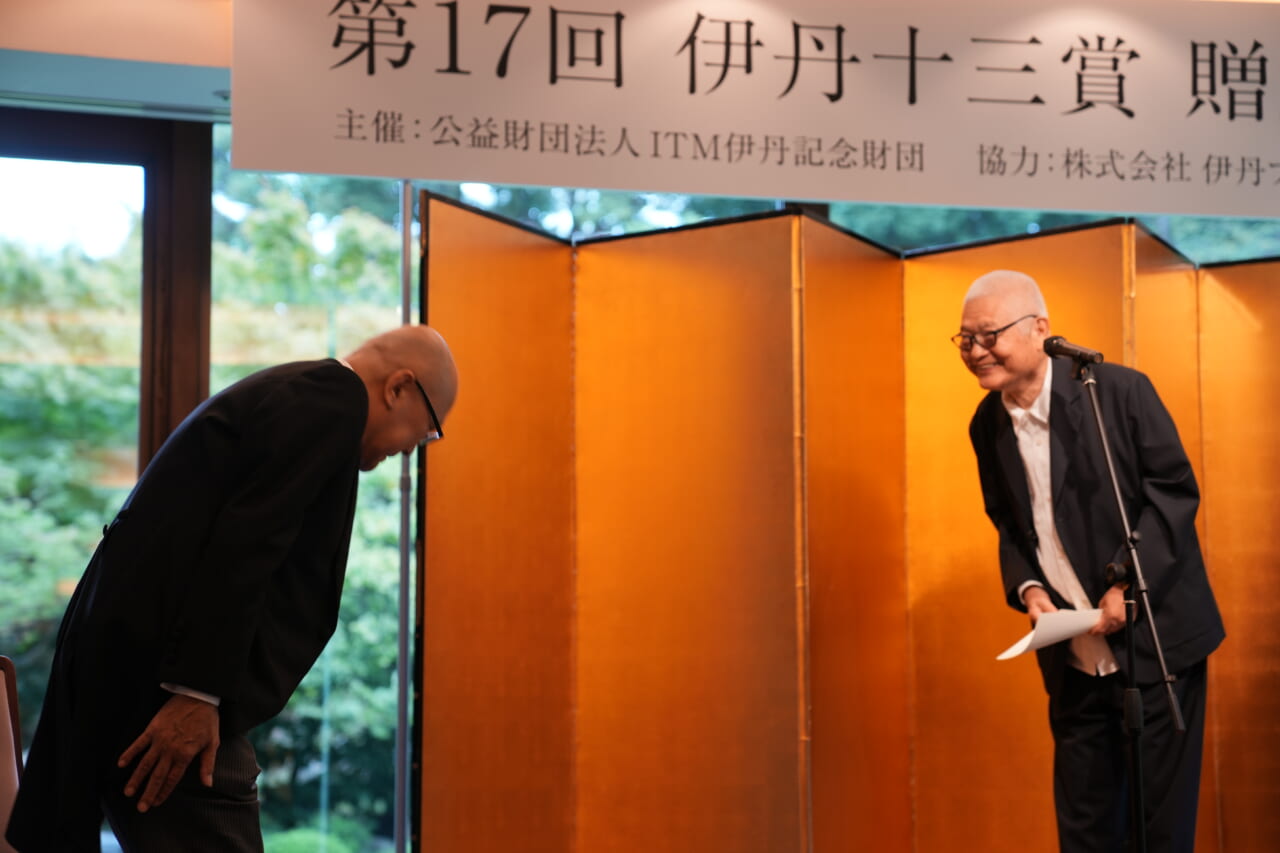 山田五郎さんが立ち上がり、壇上の南伸坊さんと笑顔でお辞儀をしあっています。