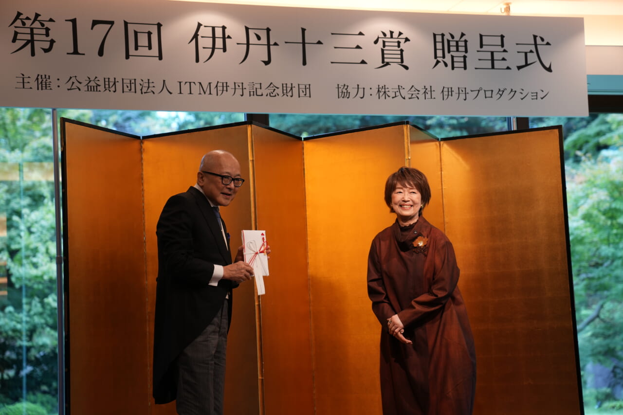 宮本信子さんが、壇上で山田五郎さんにご祝儀袋に入った副賞を手渡しています。