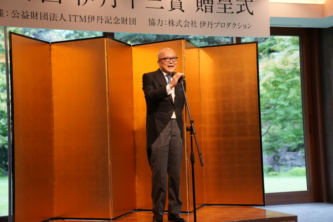 山田五郎さんが壇上で話し続けています。片手をマイクに添え、笑顔です。