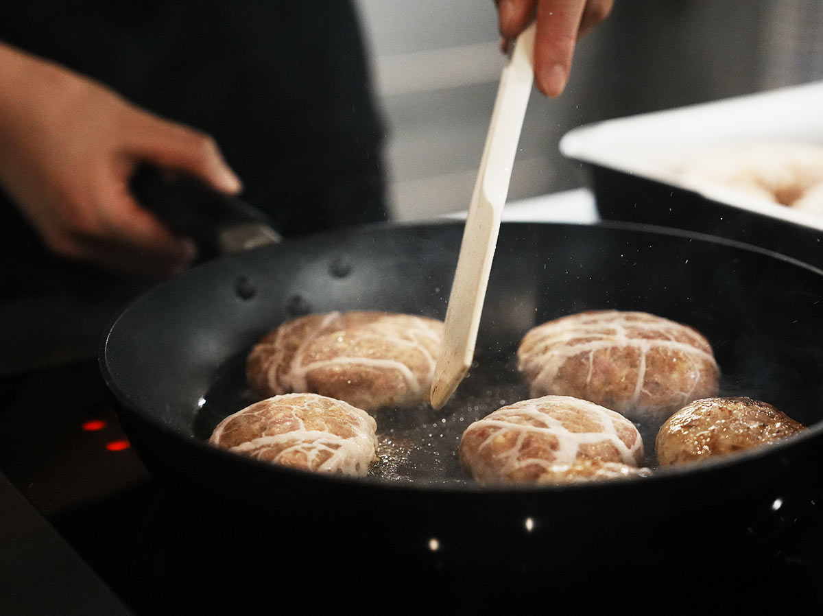 ハンバーグに網脂が巻かれて、フライパンで焼かれている