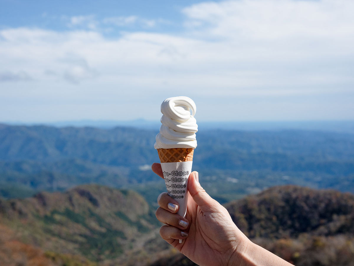 晴れた鳥居峠の青空を背にソフトクリームを手に持っている