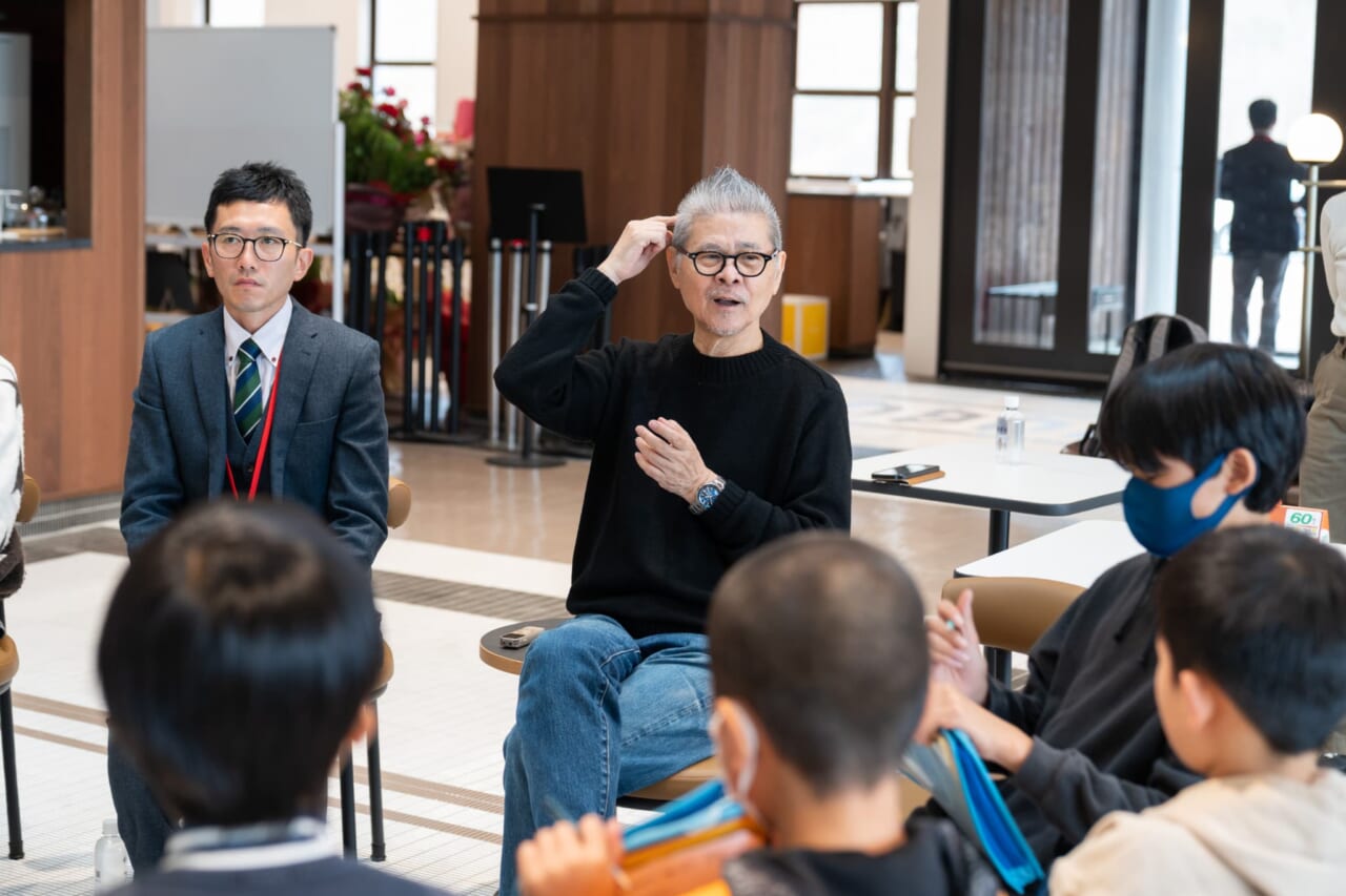 糸井が白川小のみなさんに向かって話している。手を頭に当て、「考える」ジェスチャーをしている。