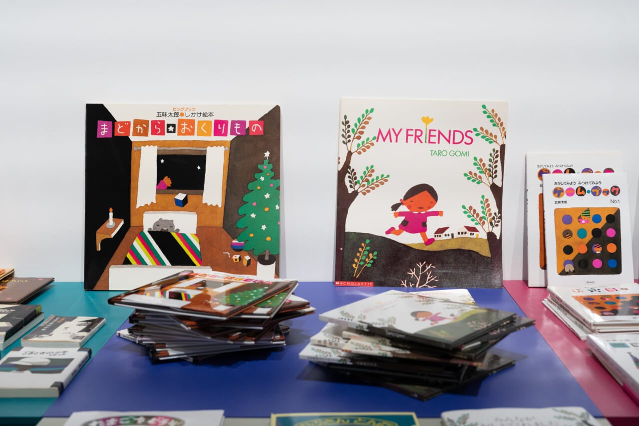 五味さんの絵本『まどからおくりもの』と、『みんながおしえてくれました』の英訳版『MY FRIENDS』が、表紙が見えるように並べられている。手前にはその２作が渦を巻くように積まれている。